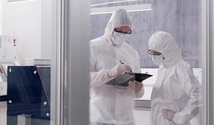 Two industrial engineers wearing protective equipment having a discussion in a factory clean room