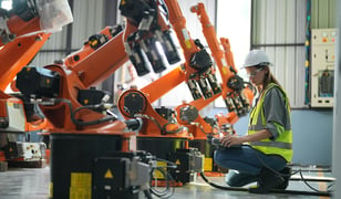 female engineer programming multiple robots in a factory