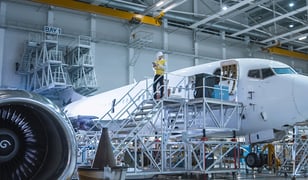 Aircraft engineer standing on stairs next to an airplane looking at a tablet