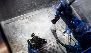 gloved worker cleaning part with high pressure spray